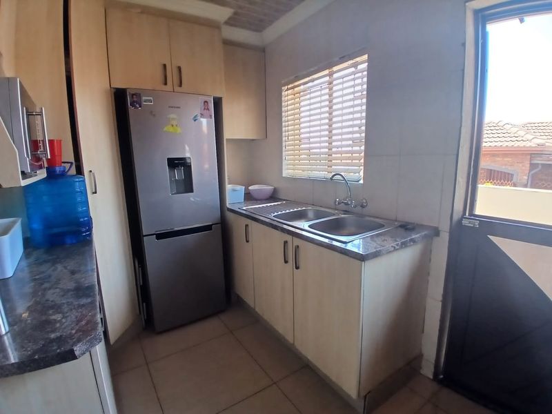 A functional scullery area featuring built-in cabinetry, a double bowl sink, laminate countertops, and tiled flooring with direct access to the exterior.