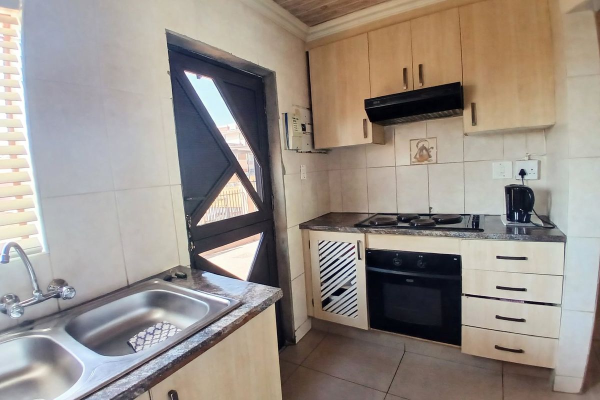 A functional kitchen featuring light wood cabinetry, a built-in oven with hob, extractor fan, and a double bowl stainless steel sink.