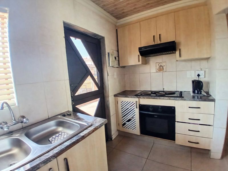 A functional kitchen featuring light wood cabinetry, a built-in oven with hob, extractor fan, and a double bowl stainless steel sink.