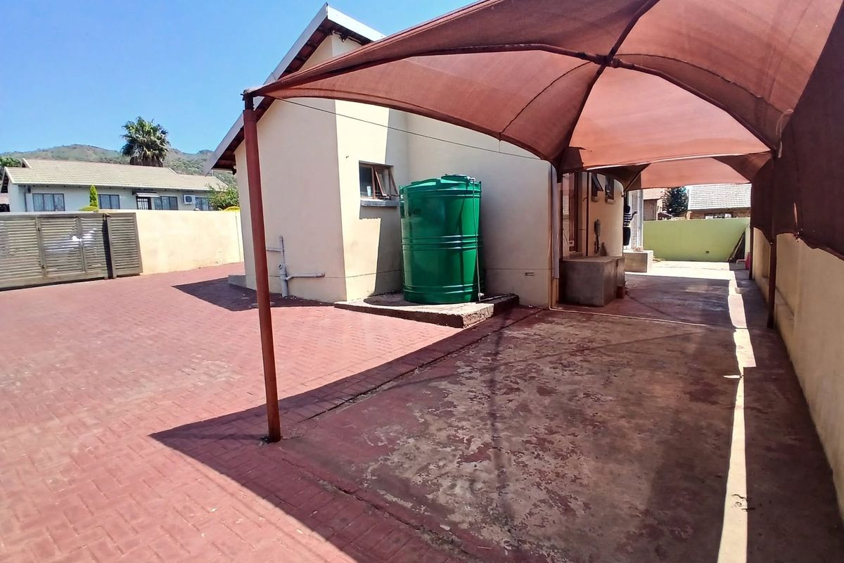 Rear exterior area featuring a paved driveway, a large shade sail structure, and a green water tank against the building wall.
