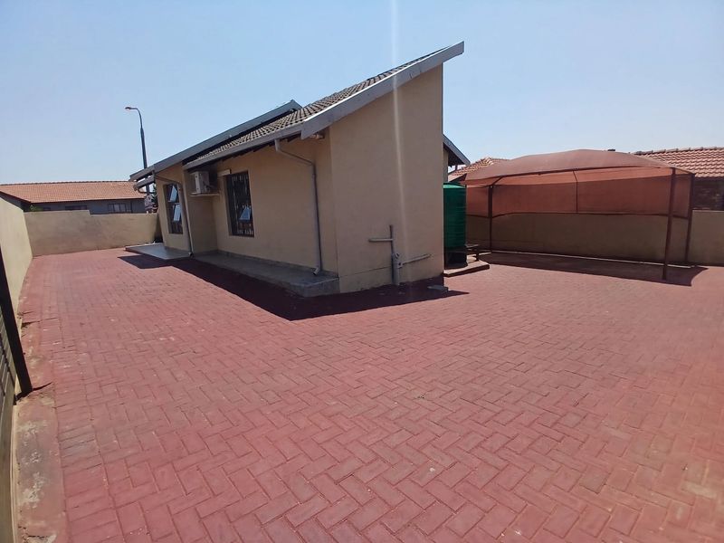 Rear exterior view of the property featuring extensive red brick paving, a perimeter wall, and a water storage tank.