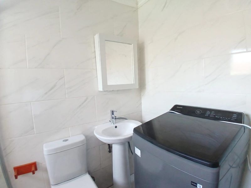 A functional laundry room featuring marble-look wall tiles, a pedestal basin, and a wall-mounted medicine cabinet.
