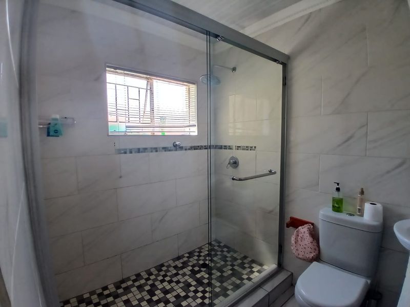 Modern bathroom featuring a glass-enclosed shower with mosaic floor tiling, marble-look wall tiles, and a standard toilet.