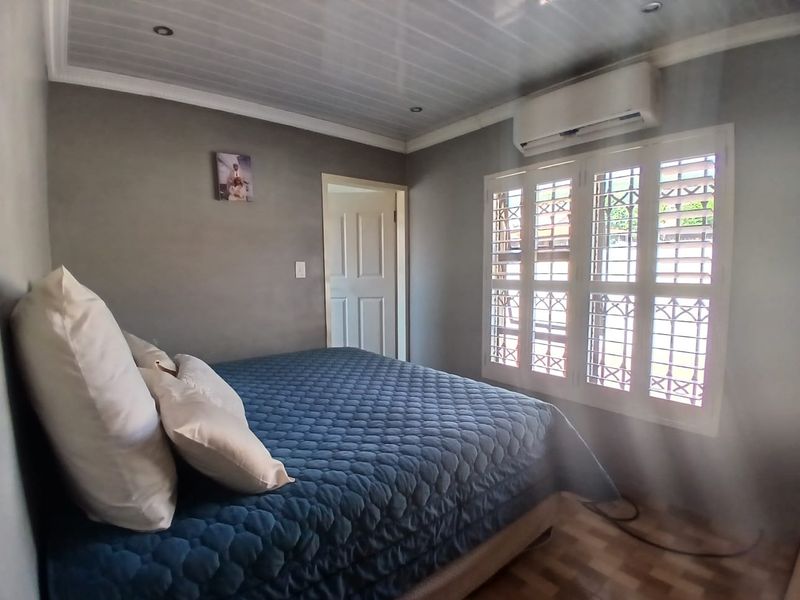 A well-maintained bedroom featuring a panelled ceiling, recessed lighting, an air conditioning unit, and plantation shutters with integrated security bars.