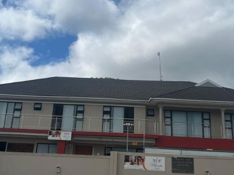 Front elevation of a two-story guest house featuring a tiled roof, upper-level balcony with metal railings, and secure perimeter wall with electric fencing.