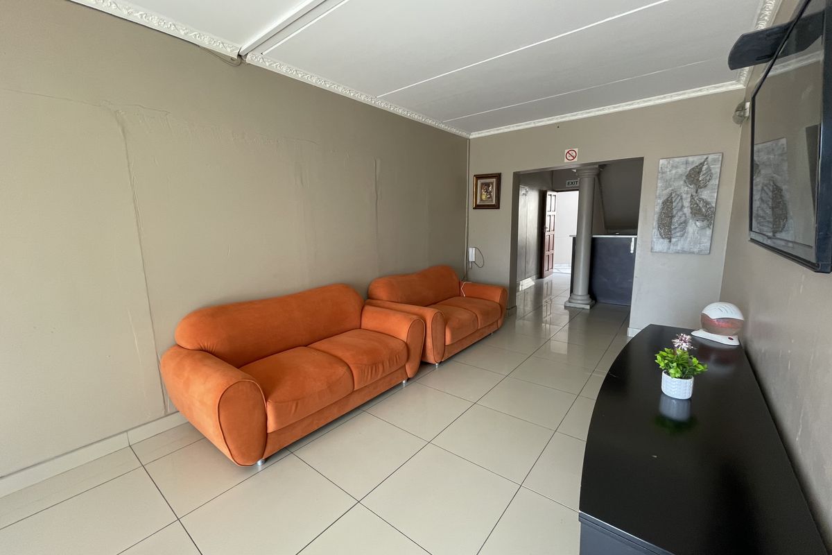 A living area featuring tiled flooring and decorative ceiling cornices, leading into a hallway with a structural column.