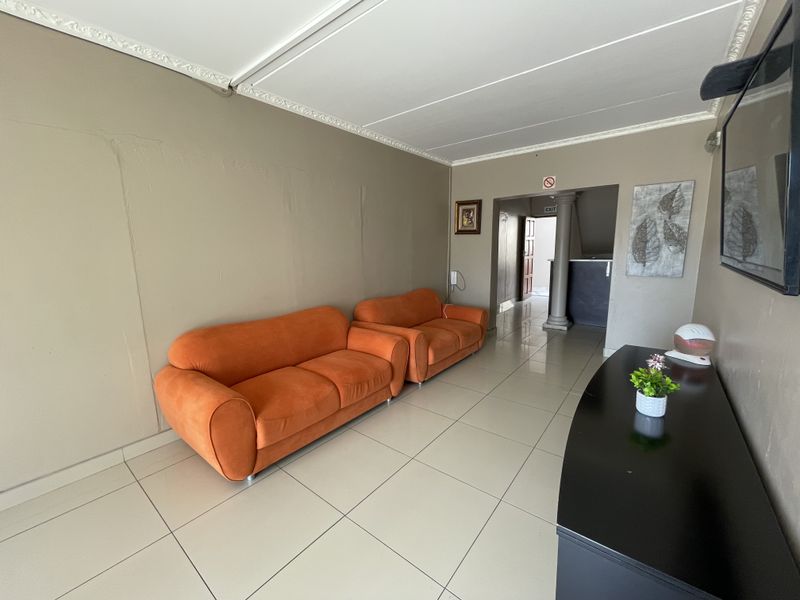 A living area featuring tiled flooring and decorative ceiling cornices, leading into a hallway with a structural column.