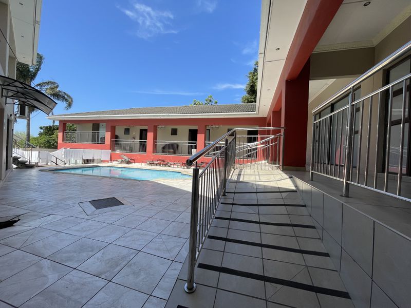 Outdoor pool area featuring a tiled patio, stainless steel safety railings, and a wheelchair-accessible ramp leading to the guest house accommodation.