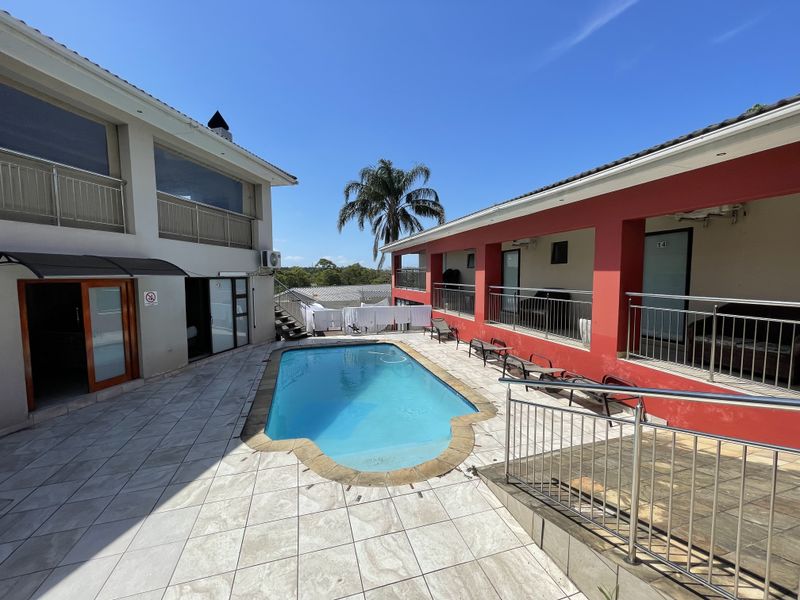 Outdoor pool area featuring a tiled deck, stainless steel safety railings, and access to guest house units with balconies.