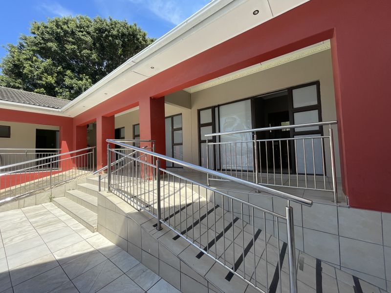 A well-maintained covered patio area featuring a tiled ramp and stairs with stainless steel handrails, providing accessible entry to the guest house.