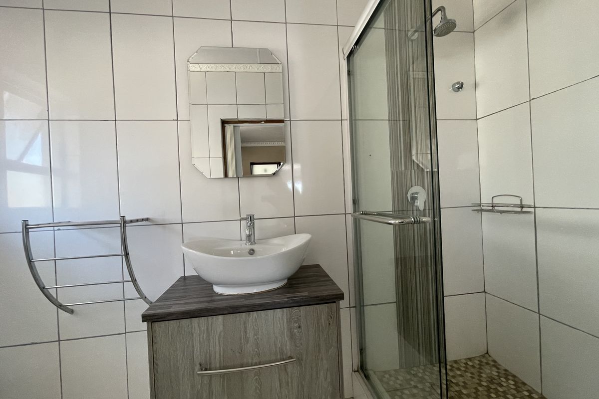 A functional bathroom featuring a vessel sink vanity, a glass-enclosed shower, and white wall tiling.