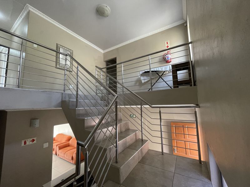 A multi-level hallway featuring a tiled staircase with a modern stainless steel balustrade and integrated safety signage.