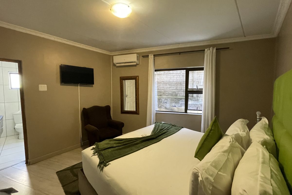 A comfortable bedroom featuring tiled flooring, an integrated air conditioning unit, and direct access to an en-suite bathroom.