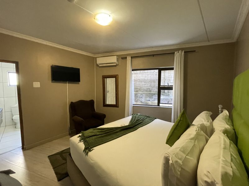 A comfortable bedroom featuring tiled flooring, an integrated air conditioning unit, and direct access to an en-suite bathroom.