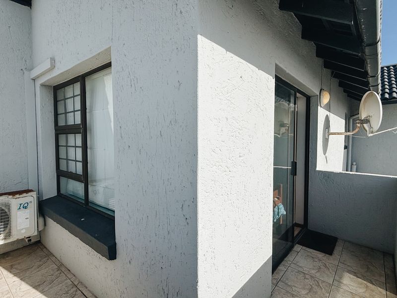 A compact balcony area featuring tiled flooring, a sliding glass door, and an external air conditioning unit mounted on the exterior wall.