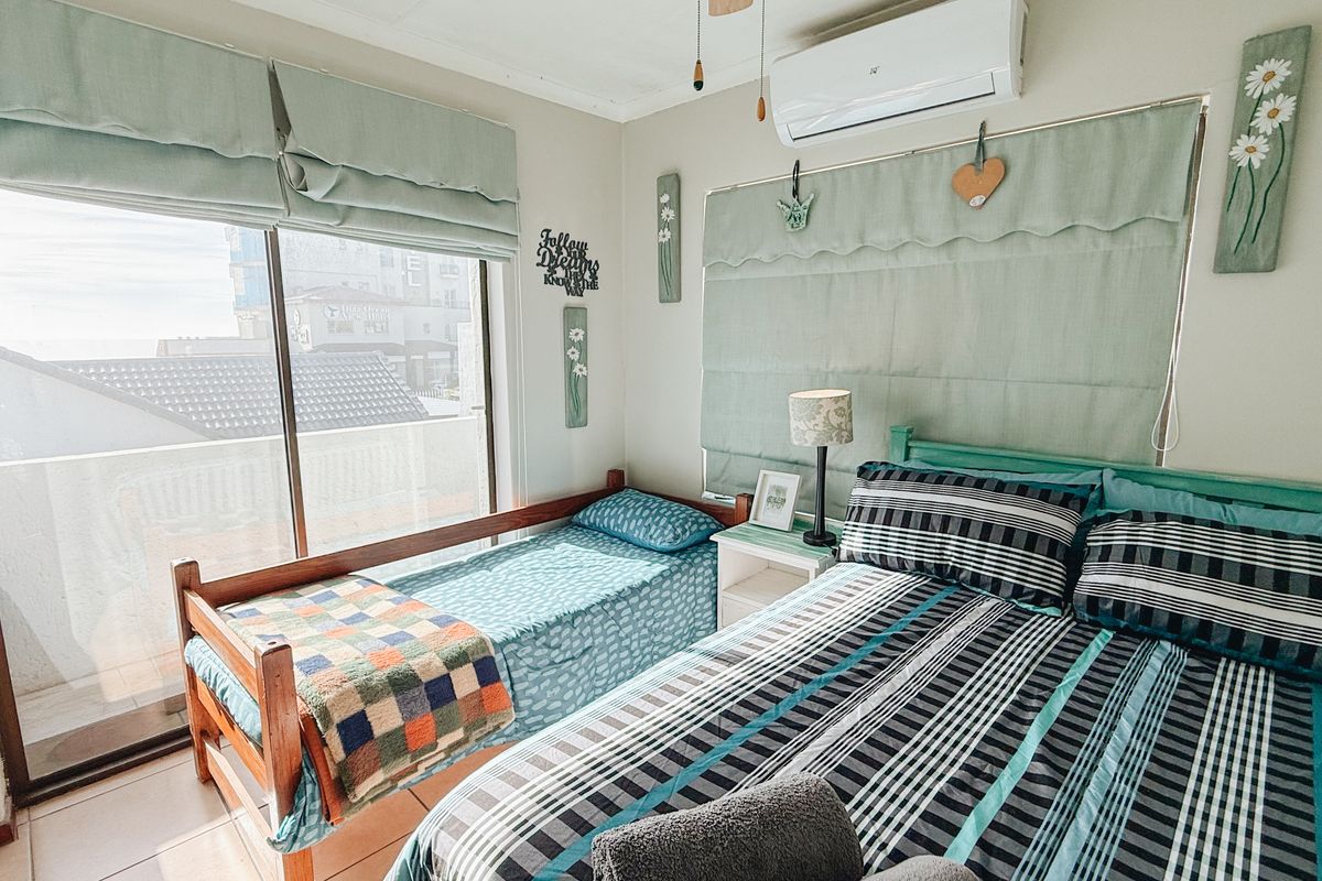 A functional bedroom featuring tiled flooring, a split-system air conditioner, and a large sliding glass door providing access to an outdoor balcony area.