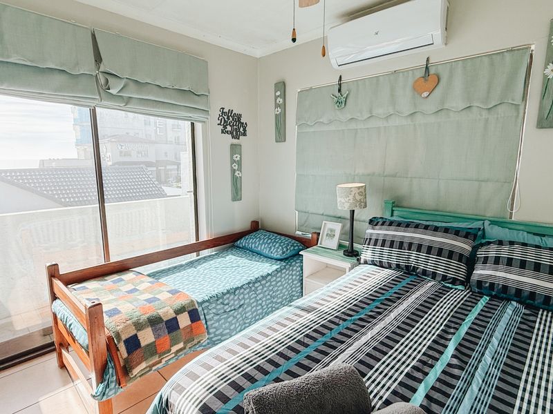 A functional bedroom featuring tiled flooring, a split-system air conditioner, and a large sliding glass door providing access to an outdoor balcony area.