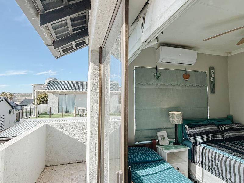 A bedroom with an adjoining balcony, featuring a ceiling fan, air conditioning unit, and sliding glass door access to an outdoor tiled area.