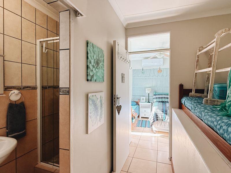 A functional bathroom featuring a tiled shower enclosure and wall-mounted basin, with a view through to an adjacent bedroom.
