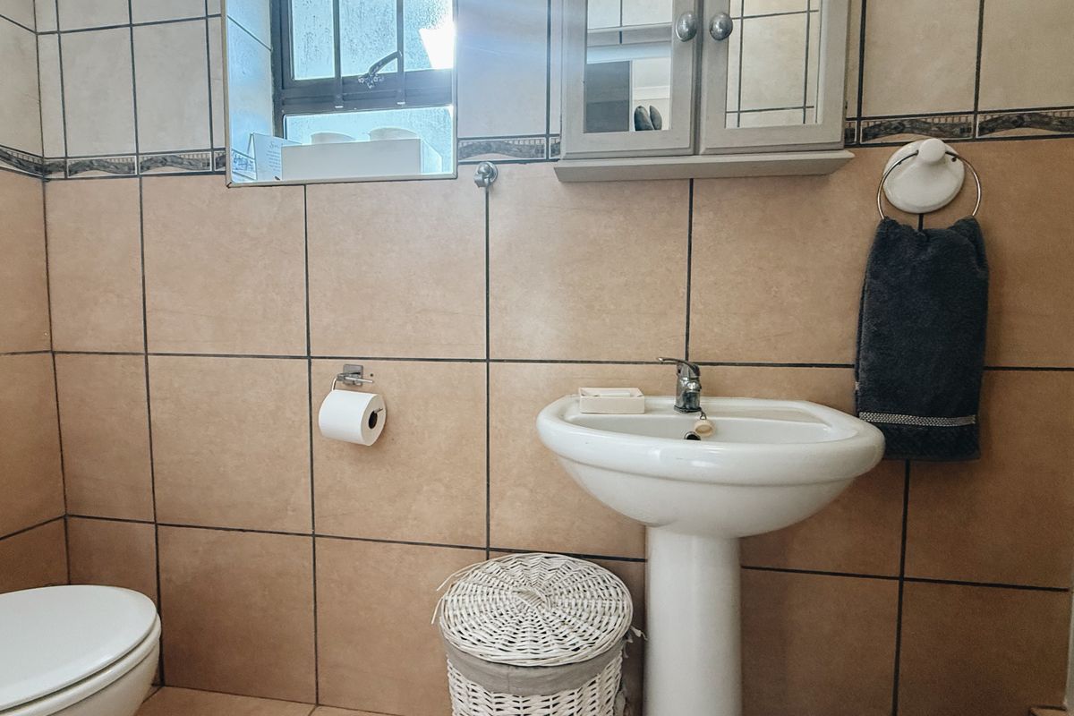 A functional bathroom featuring a pedestal basin, toilet, and wall-mounted medicine cabinet with neutral ceramic wall tiling.