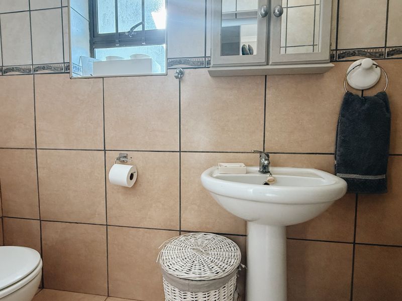 A functional bathroom featuring a pedestal basin, toilet, and wall-mounted medicine cabinet with neutral ceramic wall tiling.