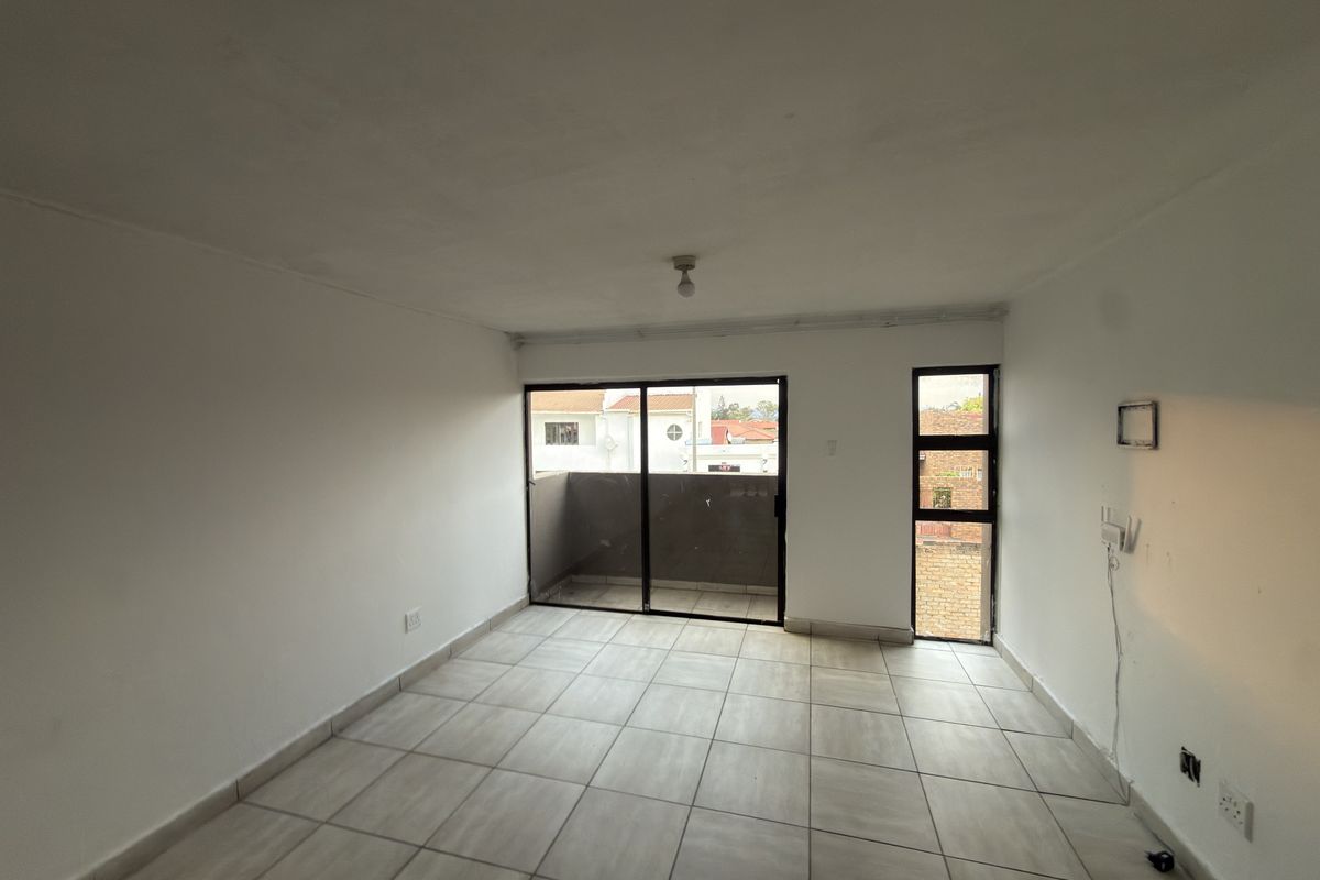 An empty living room featuring tiled flooring, a sliding glass door leading to a balcony, and natural light from a side window.