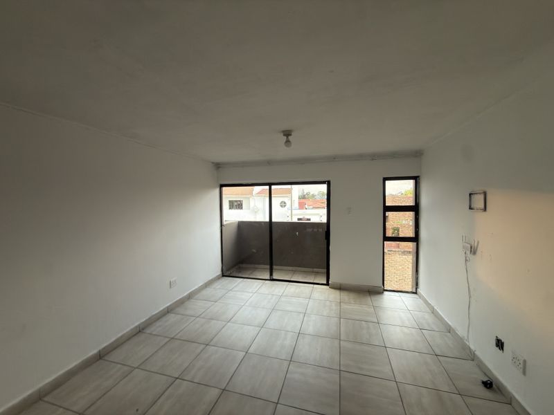An empty living room featuring tiled flooring, a sliding glass door leading to a balcony, and natural light from a side window.