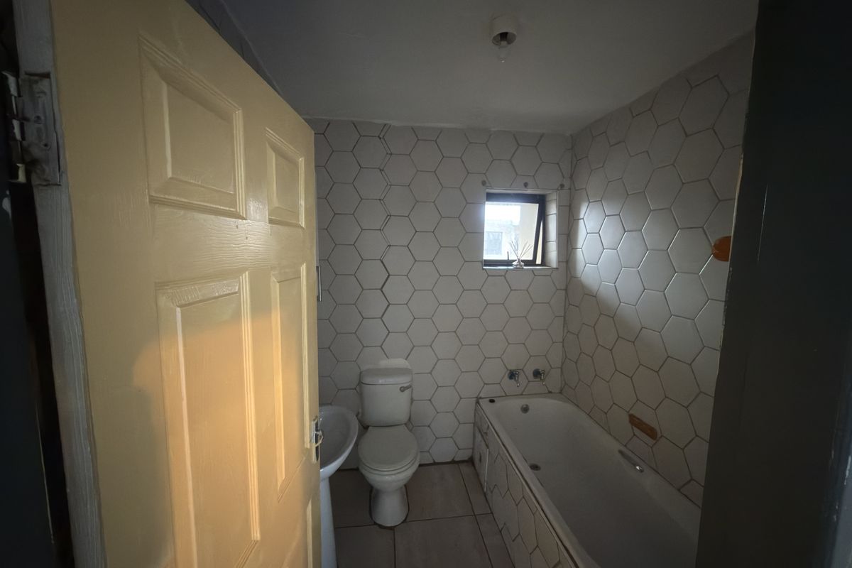 A compact bathroom featuring a bathtub, pedestal basin, toilet, and distinctive hexagonal wall tiling, requiring some cosmetic updates to improve its overall condition.