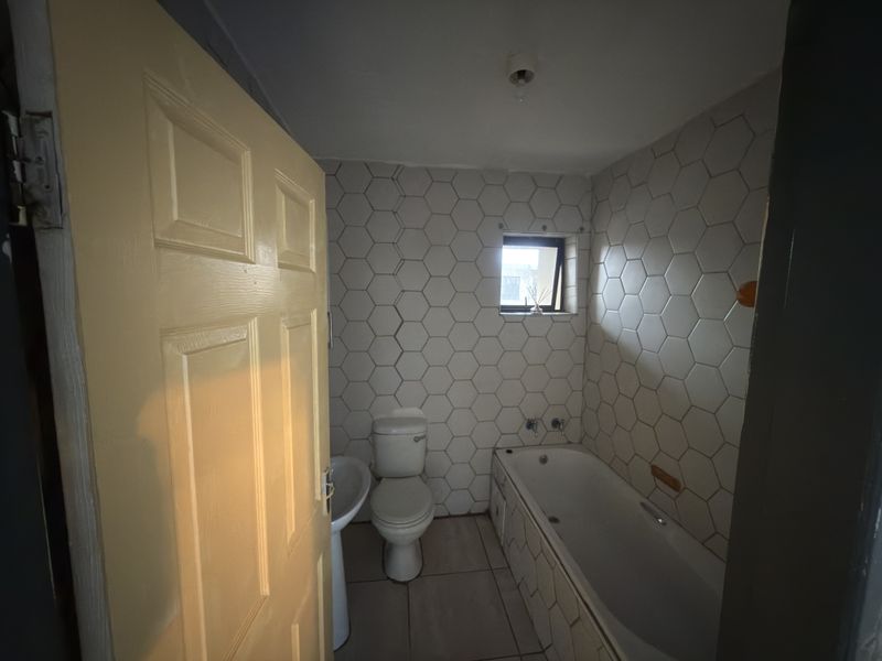 A compact bathroom featuring a bathtub, pedestal basin, toilet, and distinctive hexagonal wall tiling, requiring some cosmetic updates to improve its overall condition.