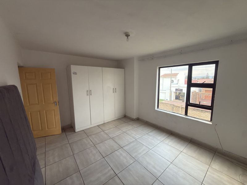A simple, empty bedroom featuring tiled flooring, a built-in wardrobe, and a large window providing natural light and street views.