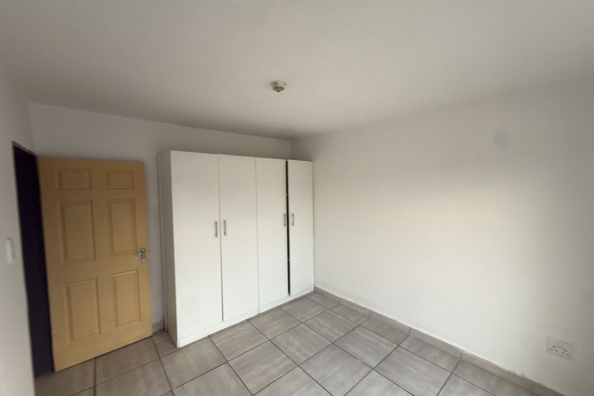 A simple, empty bedroom featuring tiled flooring and a built-in white wardrobe, providing a clean and functional space ready for personalization.