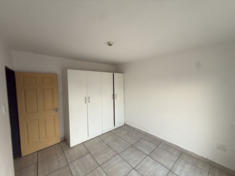 A simple, empty bedroom featuring tiled flooring and a built-in white wardrobe, providing a clean and functional space ready for personalization.