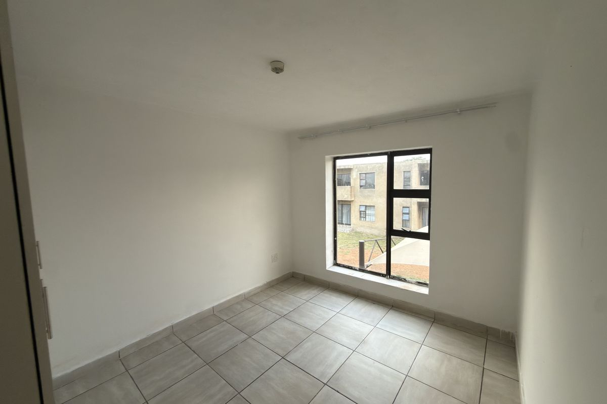 A clean, empty bedroom featuring neutral tiled flooring and a large aluminium-framed window providing natural light.