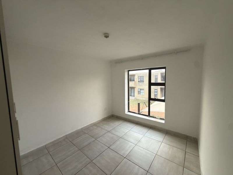 A clean, empty bedroom featuring neutral tiled flooring and a large aluminium-framed window providing natural light.