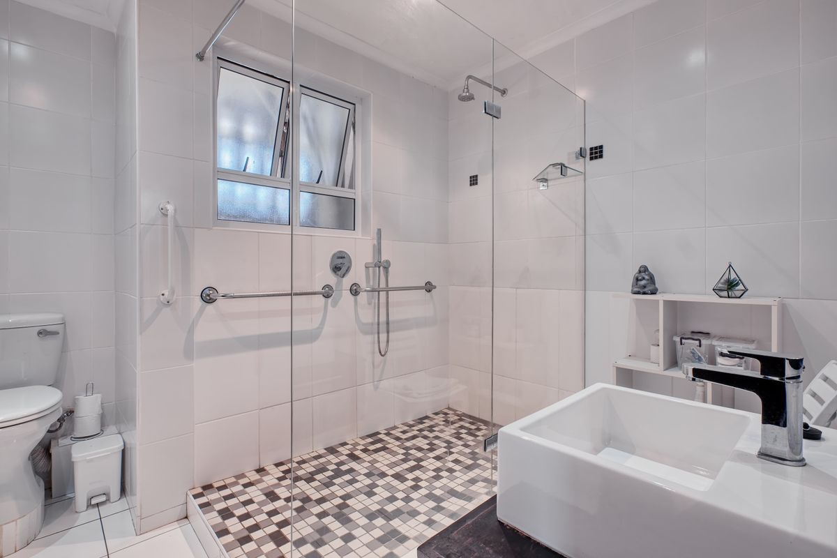 Modern bathroom featuring a walk-in shower with glass screen, wall-mounted grab rails, vessel sink, and clean white tiled finishes.