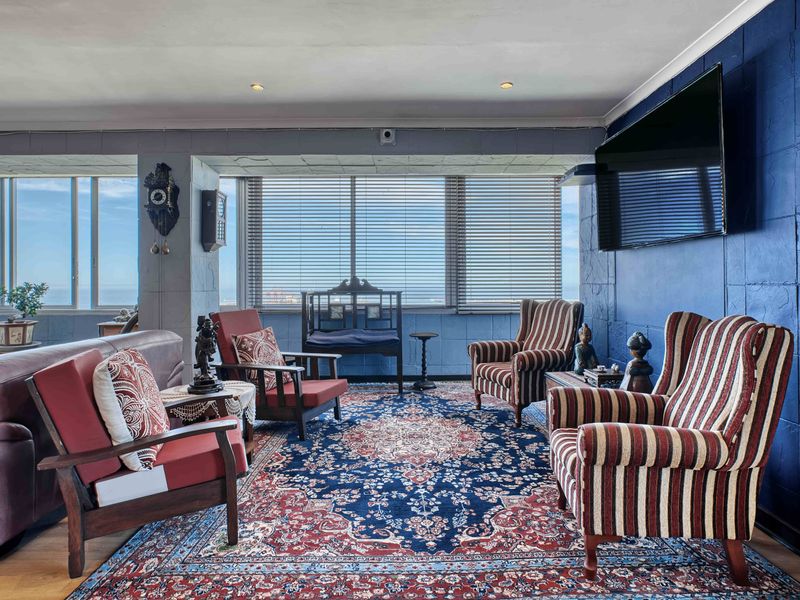 Spacious living room featuring a textured blue accent wall, large windows with venetian blinds, and recessed downlighting, offering a bright and comfortable atmosphere.