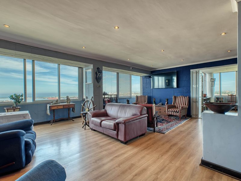 Spacious penthouse living area featuring expansive windows with panoramic coastal views, laminate flooring, and a striking blue textured feature wall.