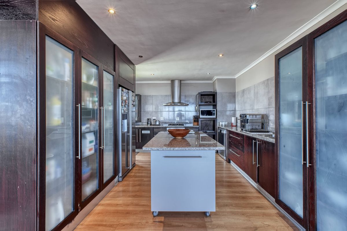 Modern kitchen featuring dark wood cabinetry, granite countertops, a central island, and integrated stainless steel appliances with ample storage behind frosted glass doors.