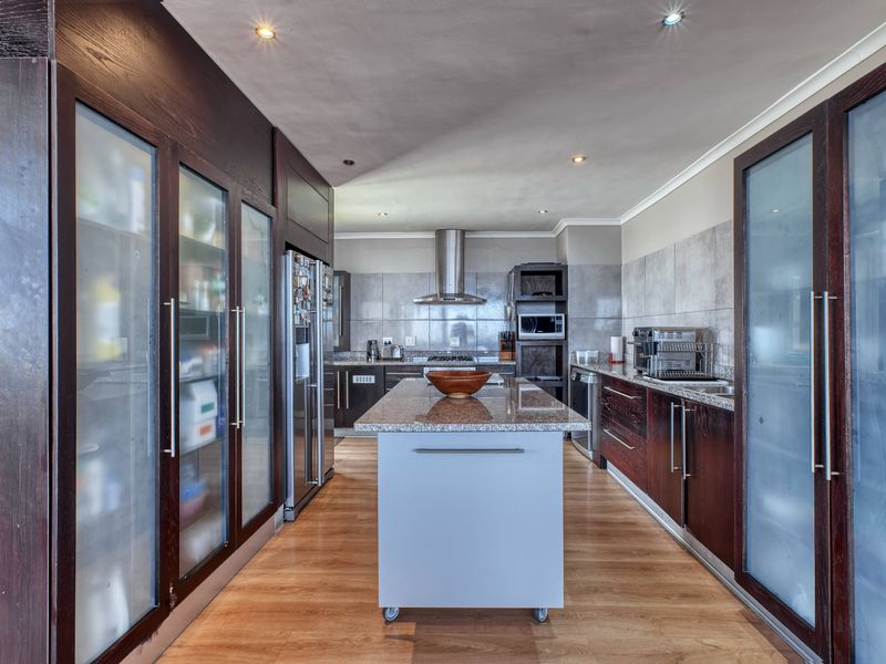 Modern kitchen featuring dark wood cabinetry, granite countertops, a central island, and integrated stainless steel appliances with ample storage behind frosted glass doors.