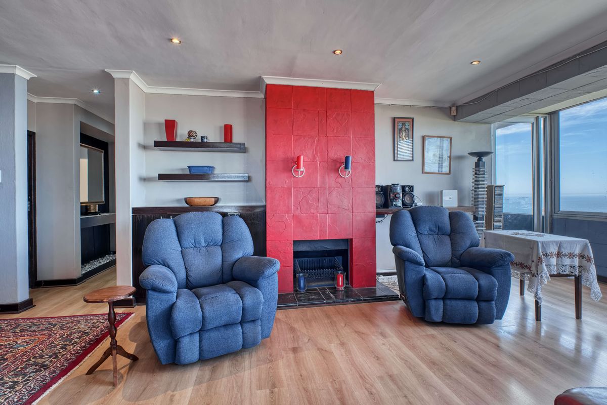 Spacious living room featuring a prominent red tiled fireplace, laminate flooring, and recessed lighting, with large windows offering natural light.