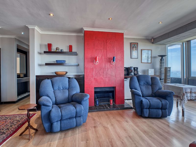 Spacious living room featuring a prominent red tiled fireplace, laminate flooring, and recessed lighting, with large windows offering natural light.