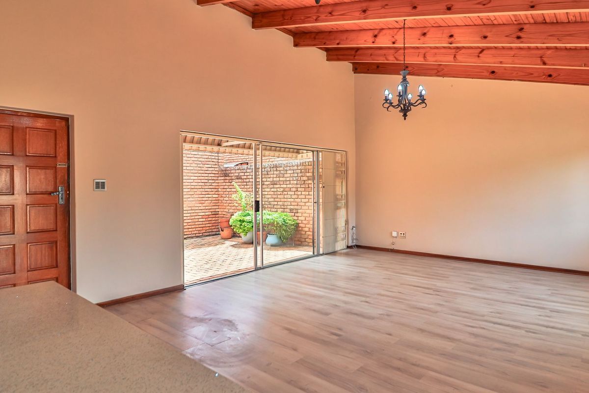 Spacious living area featuring exposed timber ceiling beams, laminate flooring, and large sliding glass doors providing access to a private courtyard.