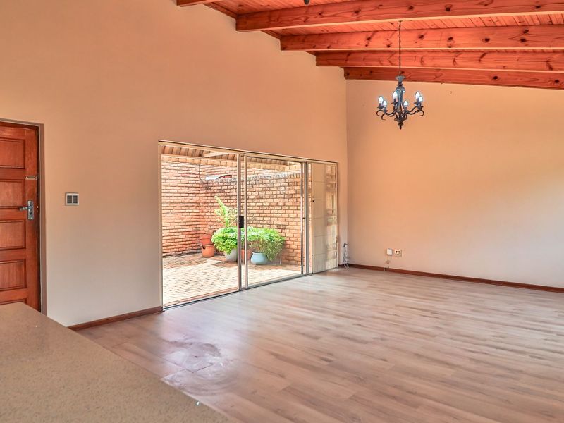 Spacious living area featuring exposed timber ceiling beams, laminate flooring, and large sliding glass doors providing access to a private courtyard.