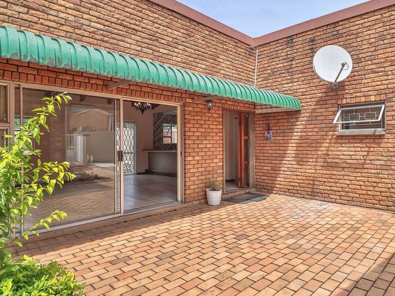 A paved outdoor patio area featuring facebrick walls, a green metal awning, and sliding glass doors providing access to the interior living space.