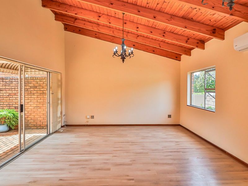 Spacious living area featuring high exposed timber beam ceilings, laminate flooring, and large sliding glass doors opening to a private patio.