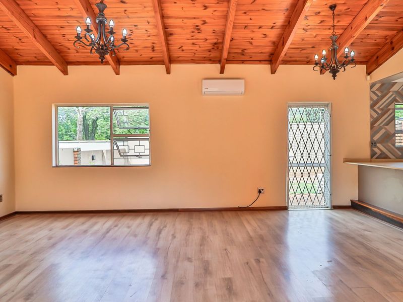 Spacious open-plan living area featuring exposed timber beam ceilings, laminate flooring, split-system air conditioning, and a breakfast bar connecting to the kitchen.