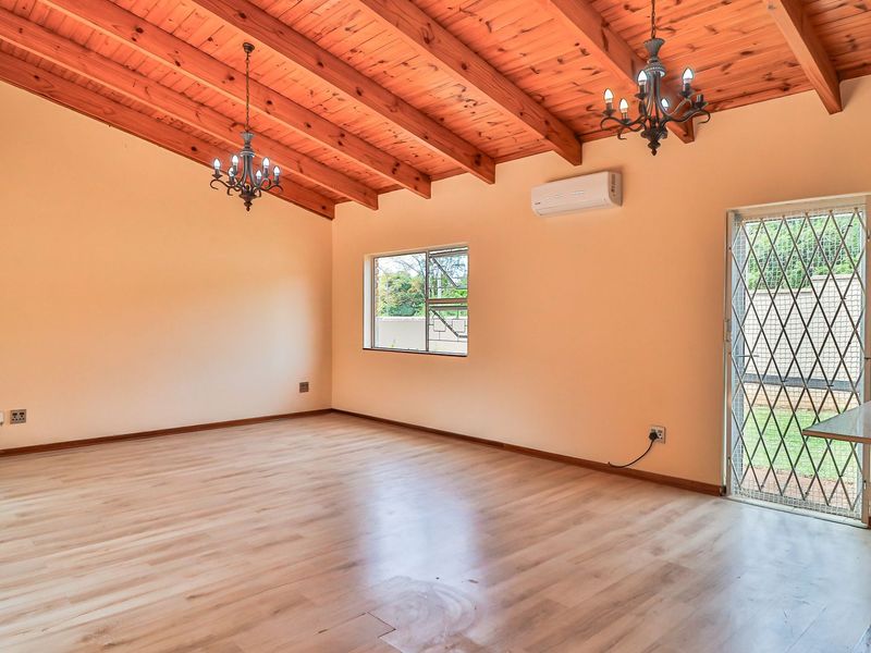 Spacious living area featuring high exposed timber beam ceilings, laminate flooring, a split-system air conditioner, and direct access to the exterior via a security gate.