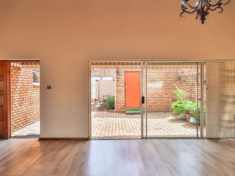 Spacious living area featuring laminate flooring, a classic timber door, and large sliding glass doors providing direct access to a private paved courtyard.