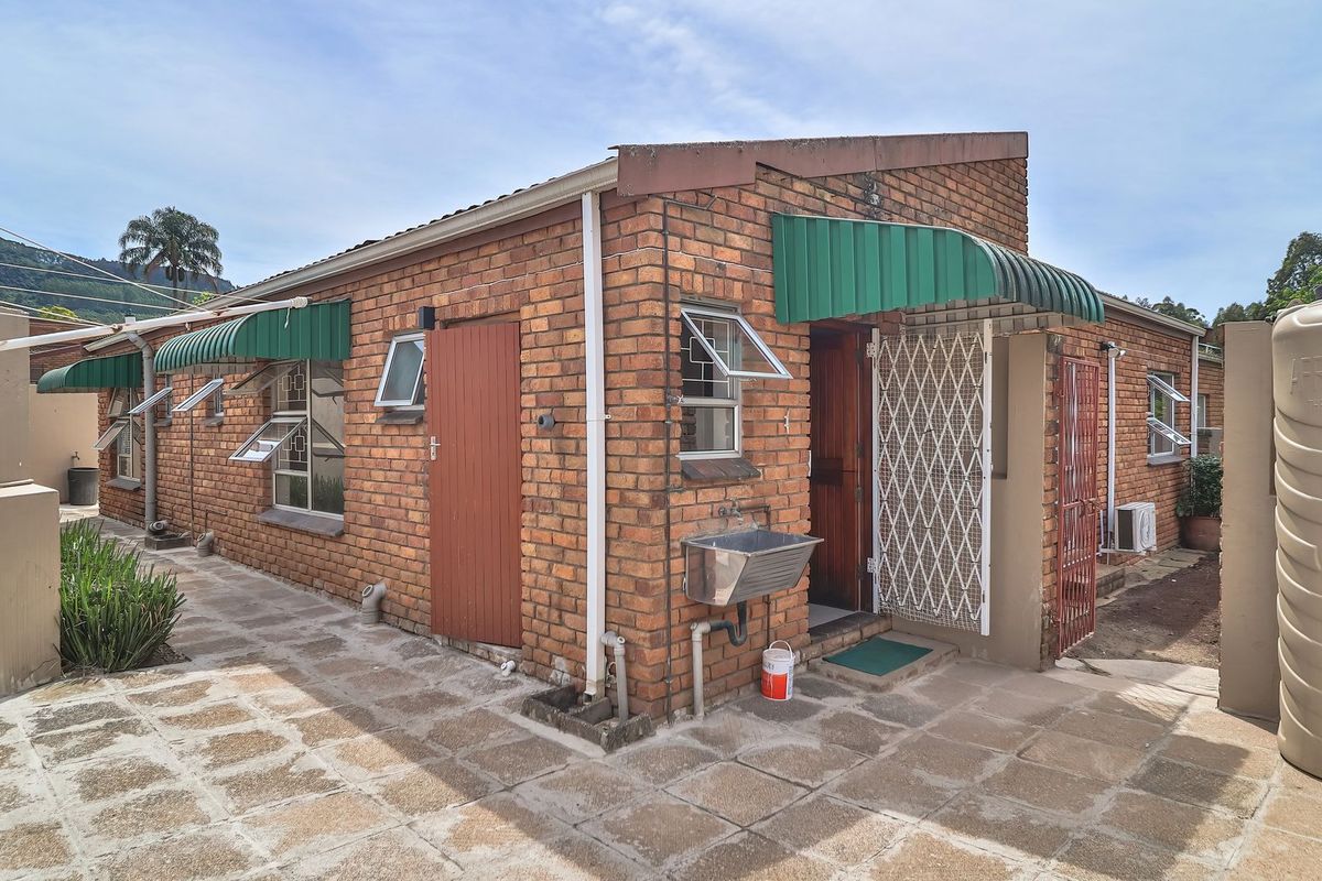Rear exterior view of a face brick townhouse featuring a paved patio, security gates, external utility sink, and a water storage tank.