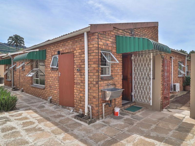 Rear exterior view of a face brick townhouse featuring a paved patio, security gates, external utility sink, and a water storage tank.